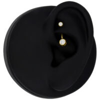 Goldenes Piercing mit klarem Kristall an schwarzem Ohrmodell