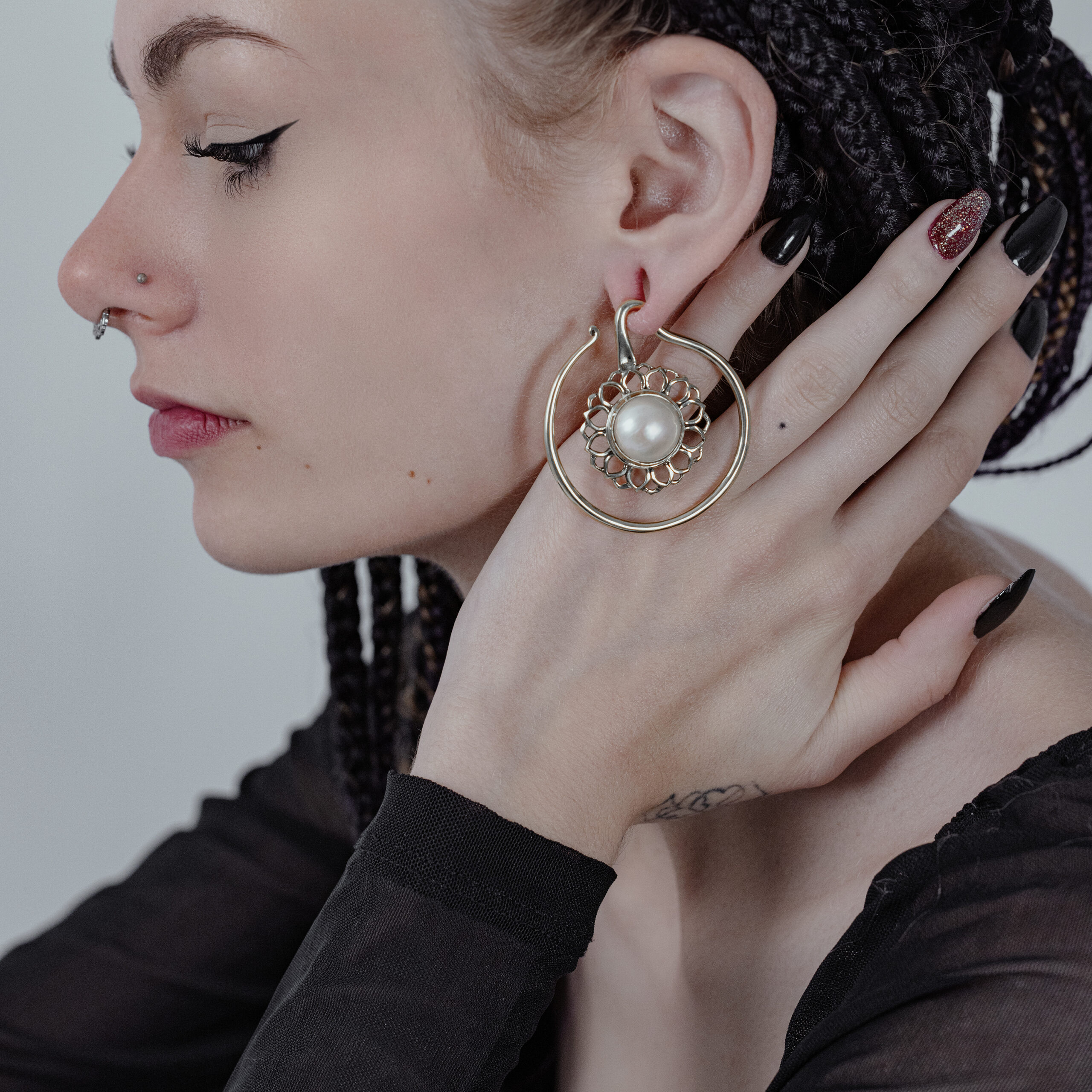 Frau mit Zopf, trägt große goldene Ohrgewichte mit weißem Onyx, Hand am Ohr