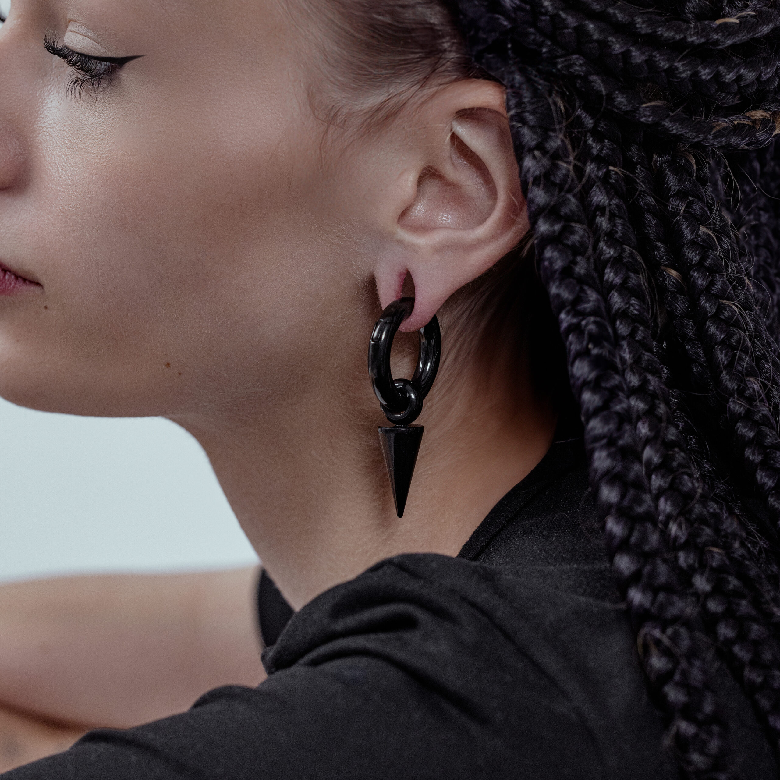 Nahaufnahme einer Person mit schwarzen Arrow Ohrgewichten aus Chirurgenstahl, Zopfhaare im Hintergrund