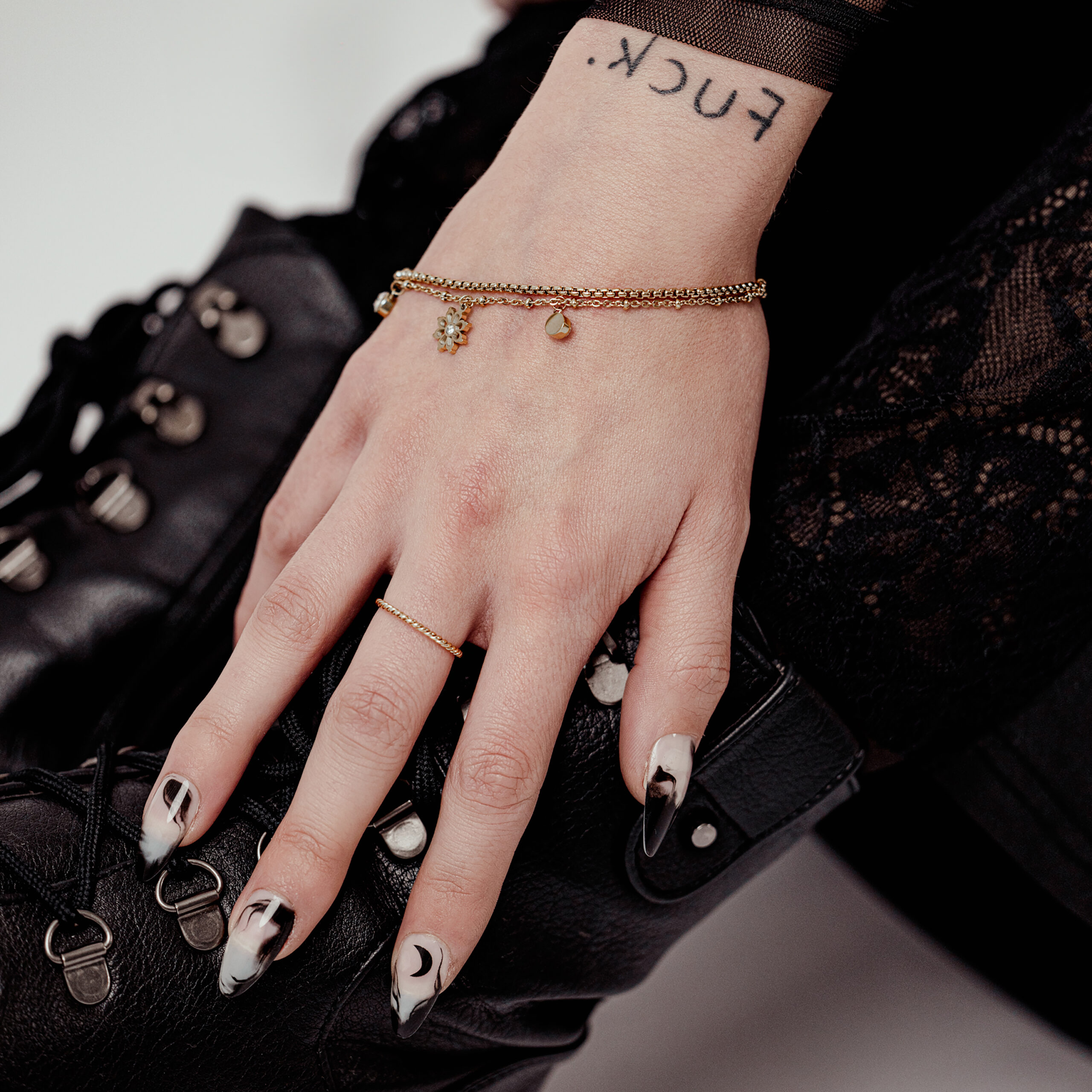 Hand mit Little Floralis Armband in Gold auf schwarzem Lederstiefel