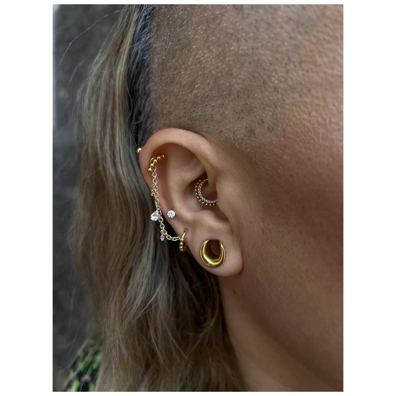 Ohr mit goldener und silberner Piercingkette, klarer Kristall