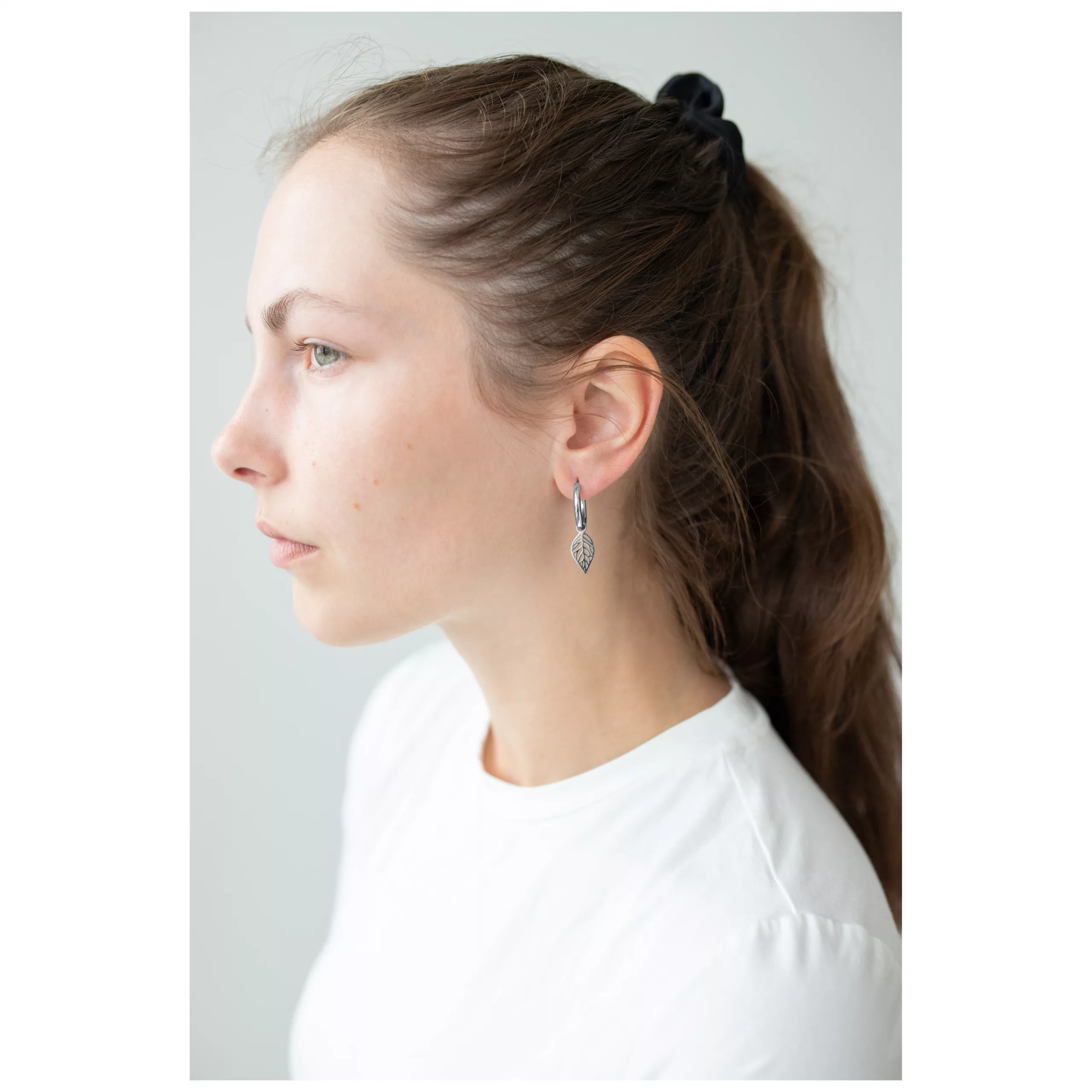 Frau mit braunen Haaren trägt silberne Little Leaf Hoops Ohrringe vor hellem Hintergrund
