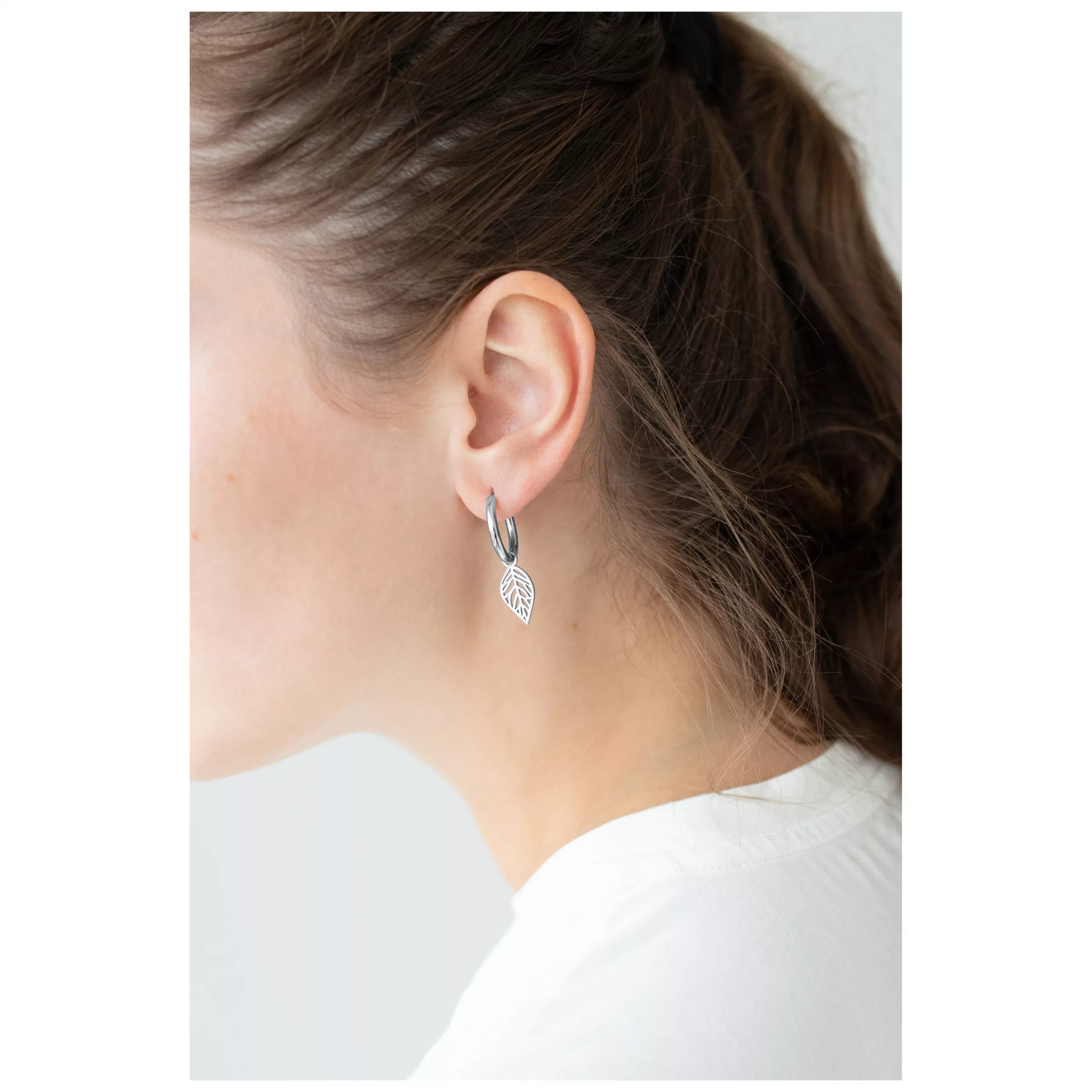 Silberne Ohrringe in Blatt-Design aus Chirurgenstahl am Ohr einer Frau mit braunem Haar