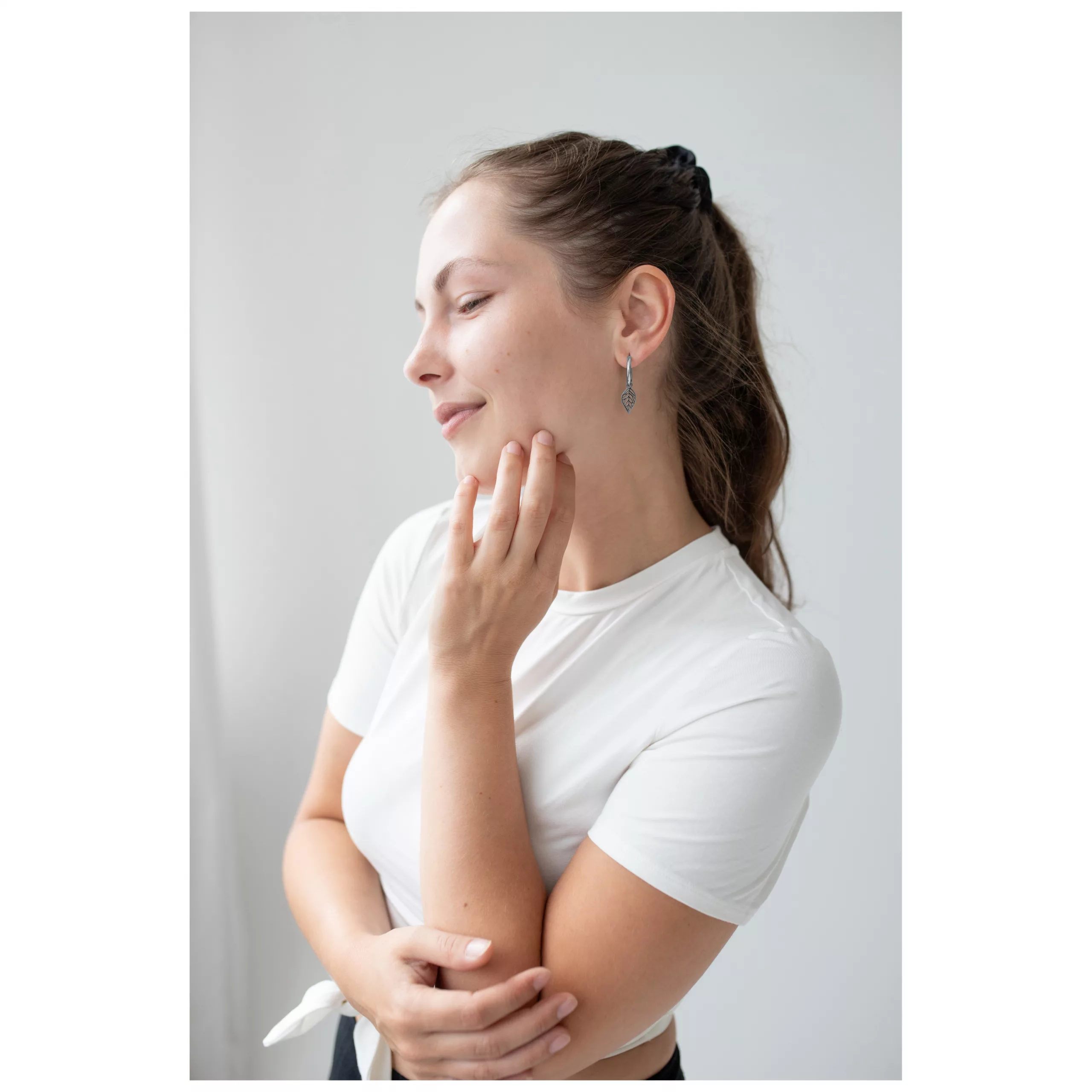 Frau mit braunem Haar trägt silberne Ohrringe in Blattform vor weißem Hintergrund