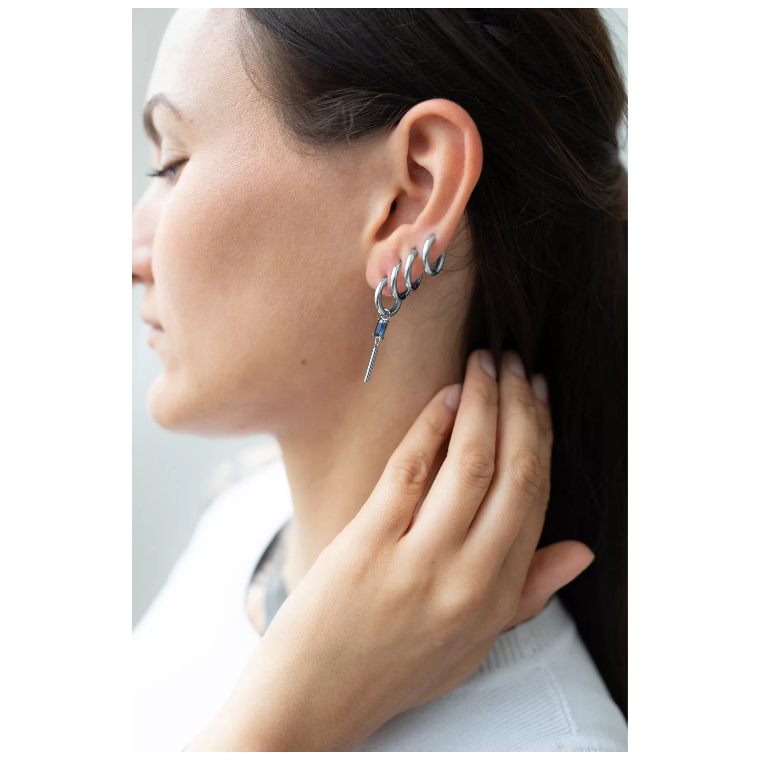 Silberne Creolen mit quadratischen Kristallen am Ohr einer Frau, seitliches Profil