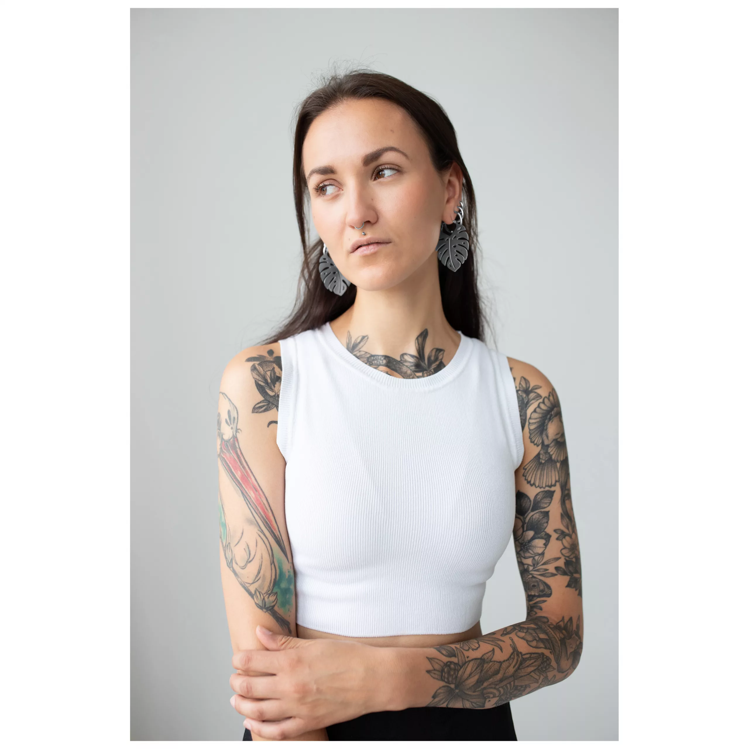 Frau mit tätowierten Armen trägt Monstera Leaf Hoops Ohrringe, weißes Top