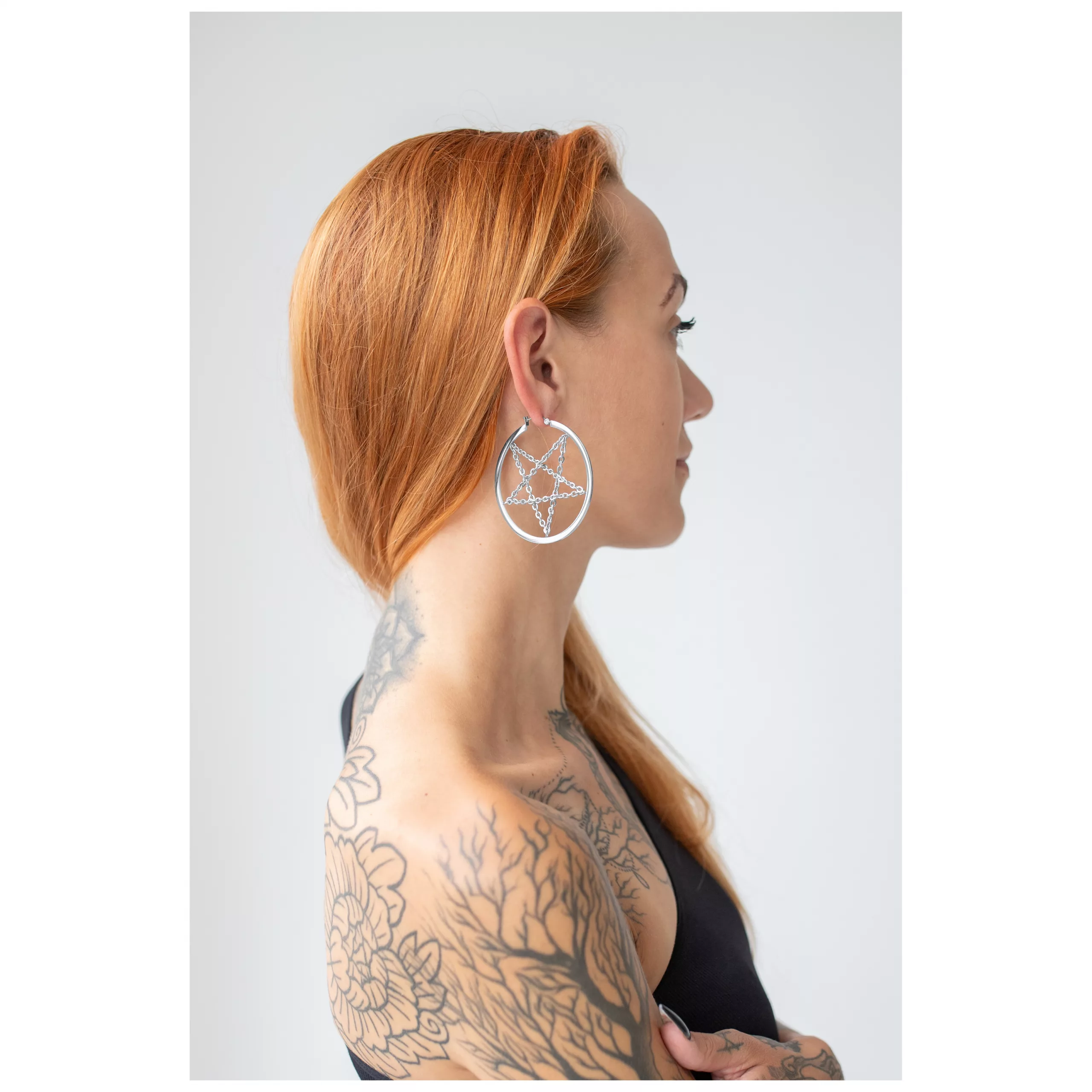Silberne Pentagramm-Ohrringe getragen von Frau mit roten Haaren vor weißem Hintergrund