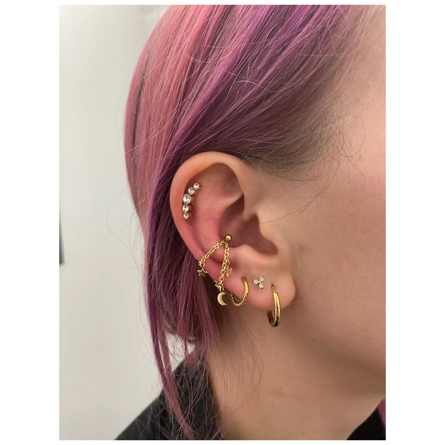 Goldene Piercingkette mit Mond- und Sternmotiven am Ohr getragen