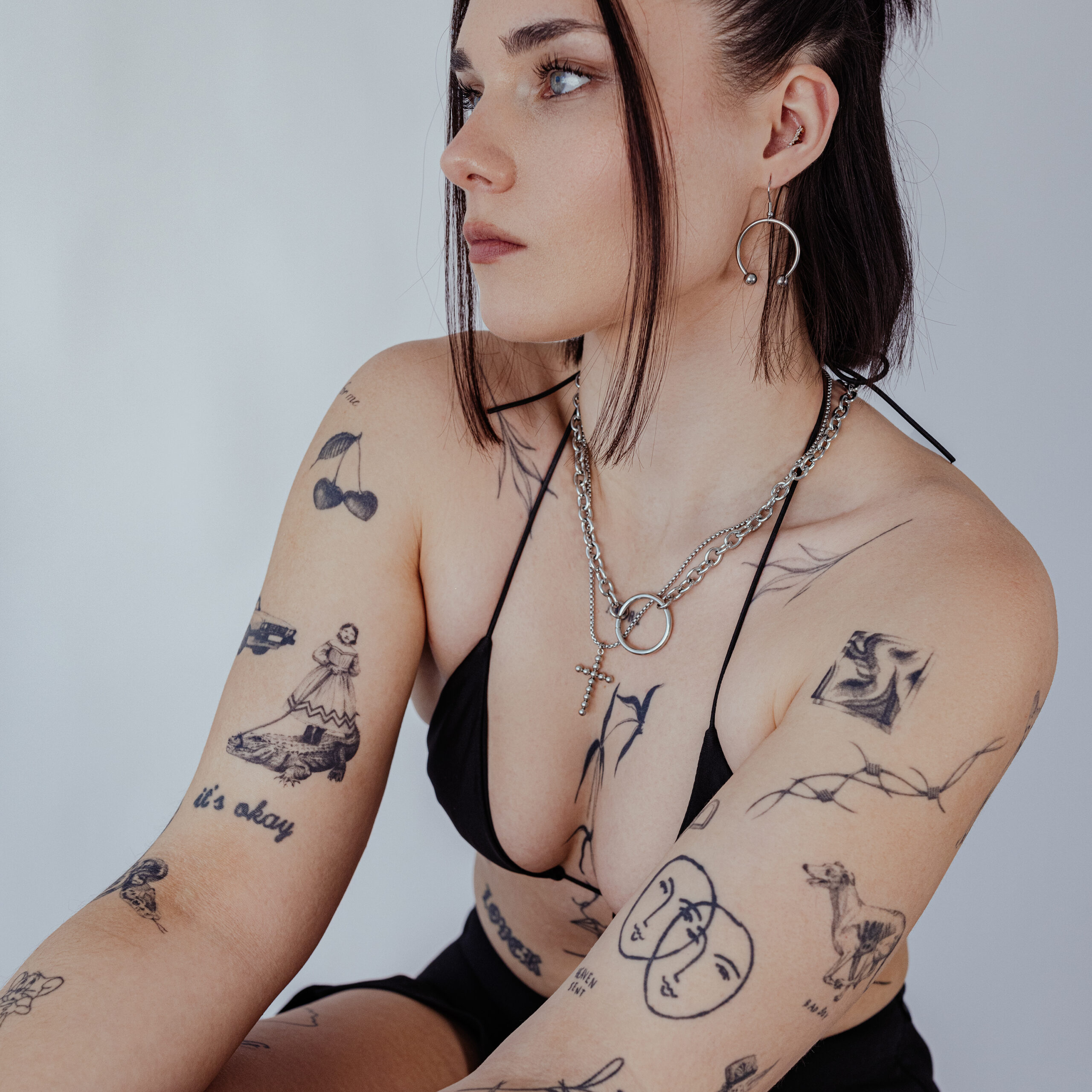 Frau mit silbernen Circular Barbell Ohrringen und Tattoos auf hellem Hintergrund