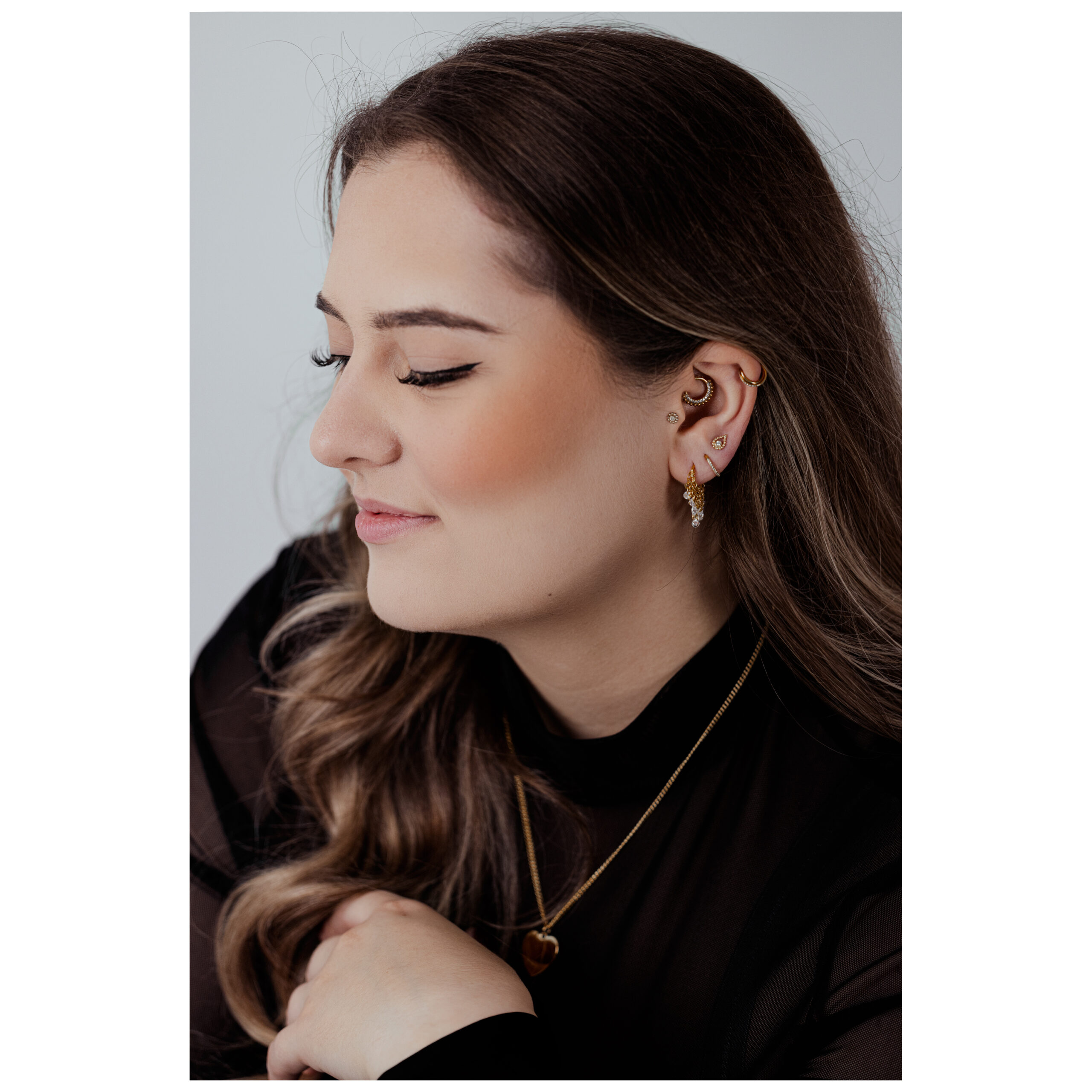 Frau mit geschlossenen Augen trägt roségoldenen Wasserfall-Kristall-Clicker im Ohr, vor grauem Hintergrund
