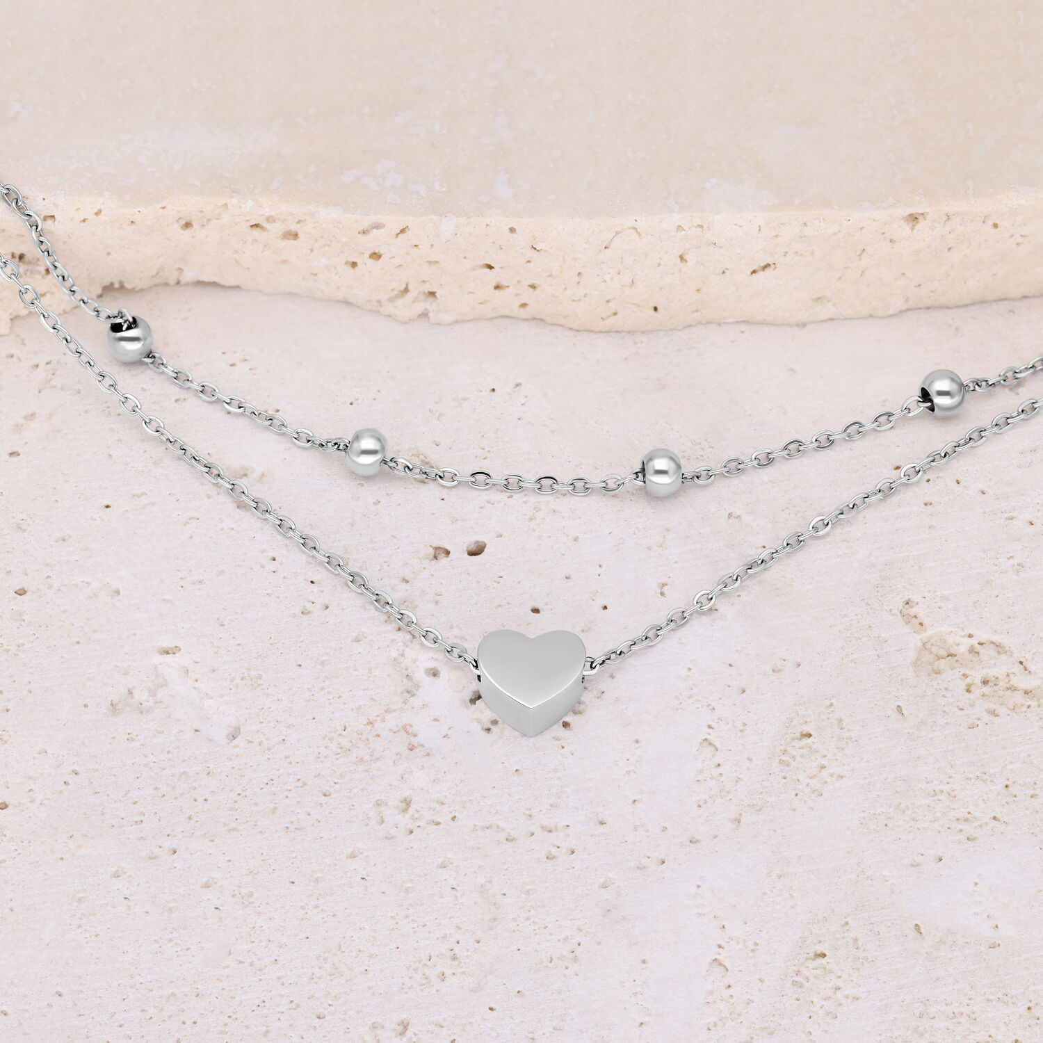 Silbernes doppelreihiges Armband mit Herz und Kugeln auf hellem Hintergrund