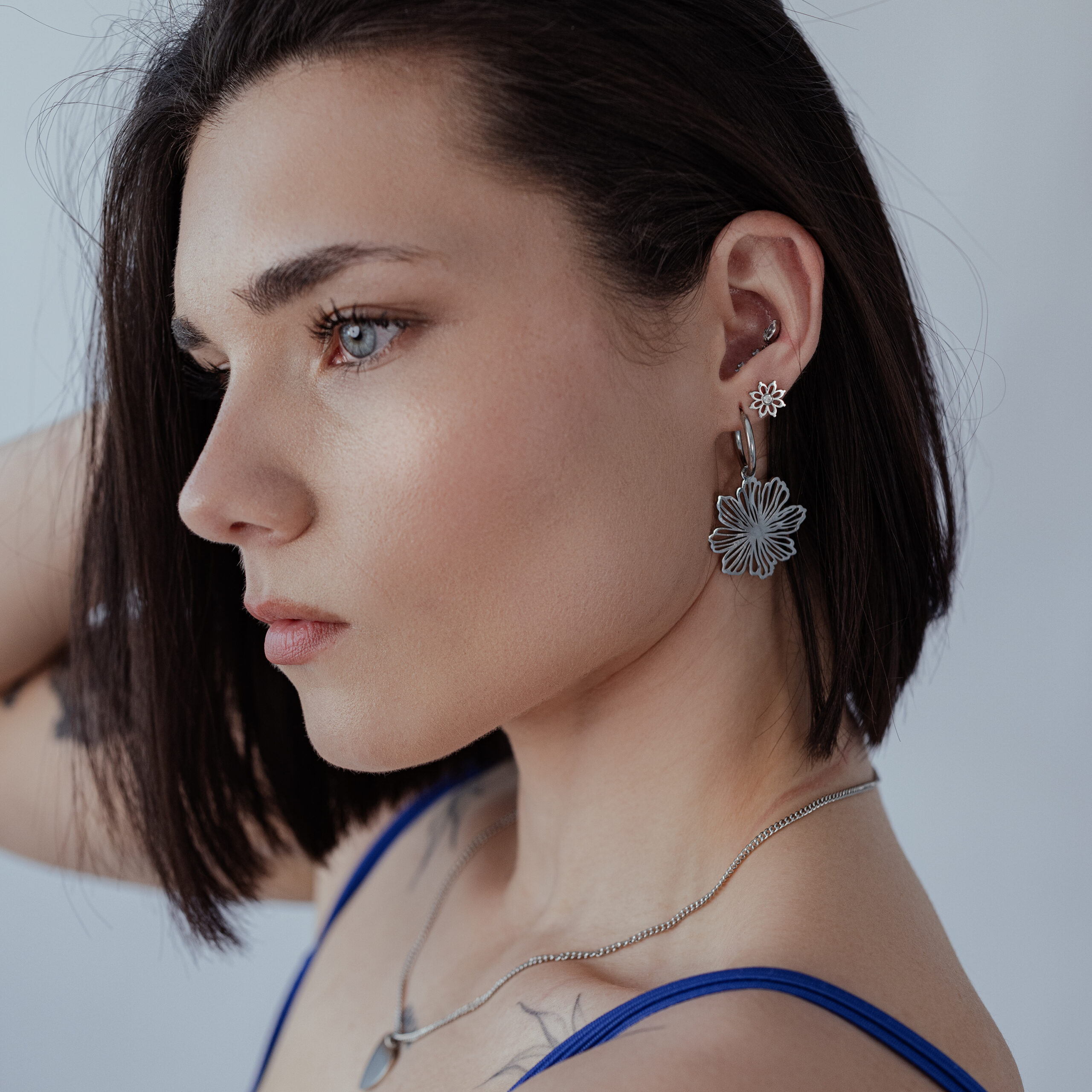Frau mit kurzen Haaren trägt silberne Fine Flower Hoops vor grauem Hintergrund