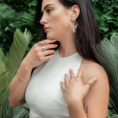 Frau mit eleganten Hängeplatten-Ohrringen aus Chirurgenstahl in tropischer Umgebung