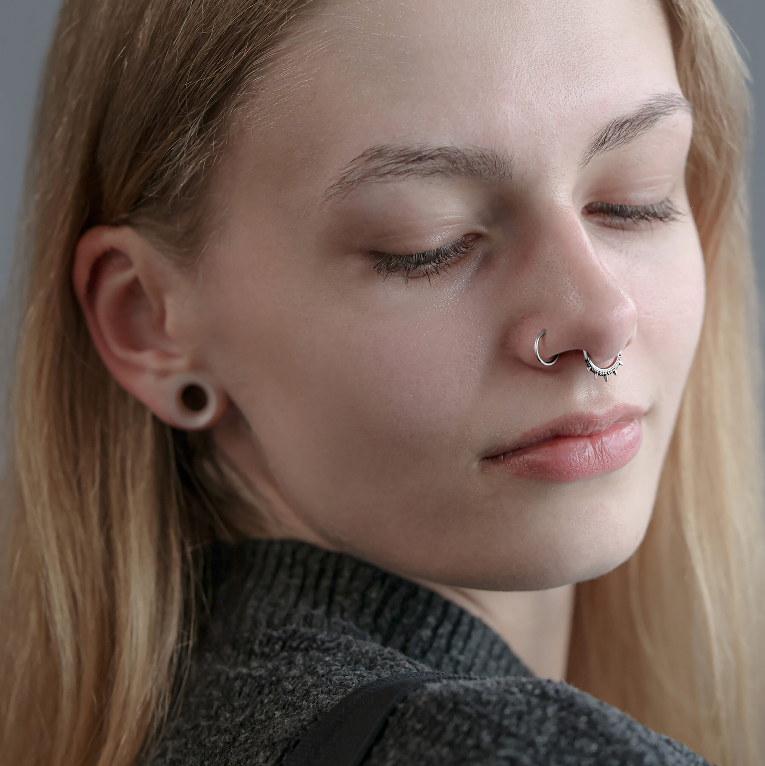 Frau mit silbernem Septum Clicker und gedehnten Ohrläppchen auf grauem Hintergrund