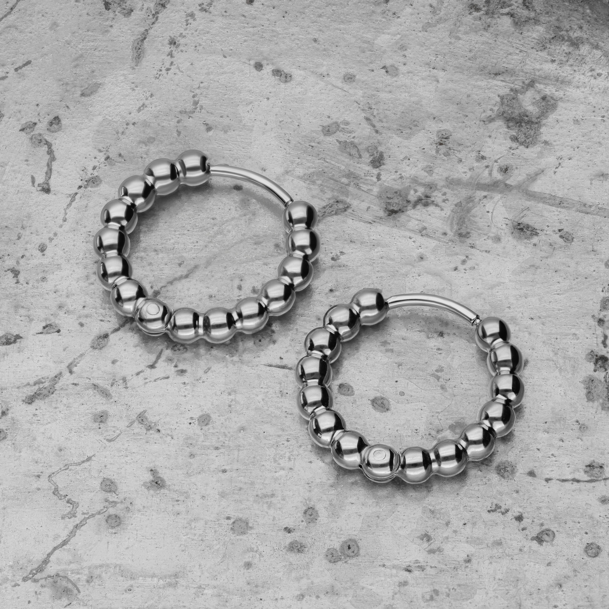 Zwei silberne Bubble Hoops Ohrringe aus Edelstahl auf grauem Betonhintergrund
