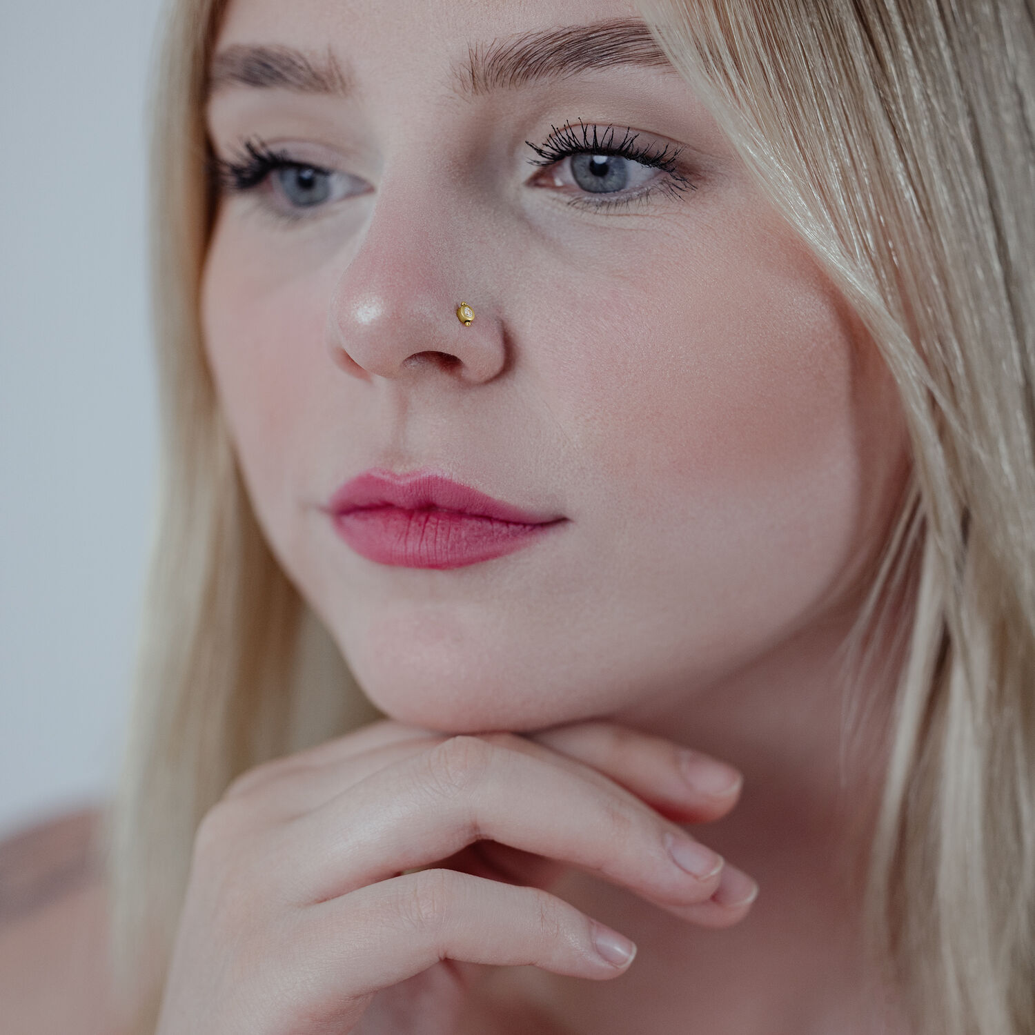 Goldener Nasenstecker in der Nase einer Frau, blondes Haar, neutraler Hintergrund