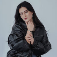 Frau mit schwarzer Lederjacke trägt silbernen Kettenring und passendes Armband auf grauem Hintergrund