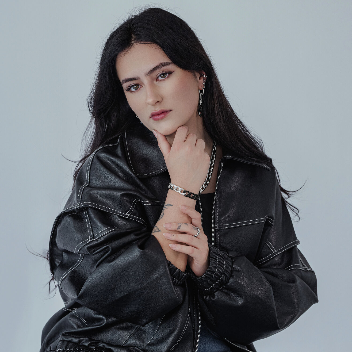 Frau mit schwarzer Lederjacke trägt silbernen Kettenring und passendes Armband auf grauem Hintergrund