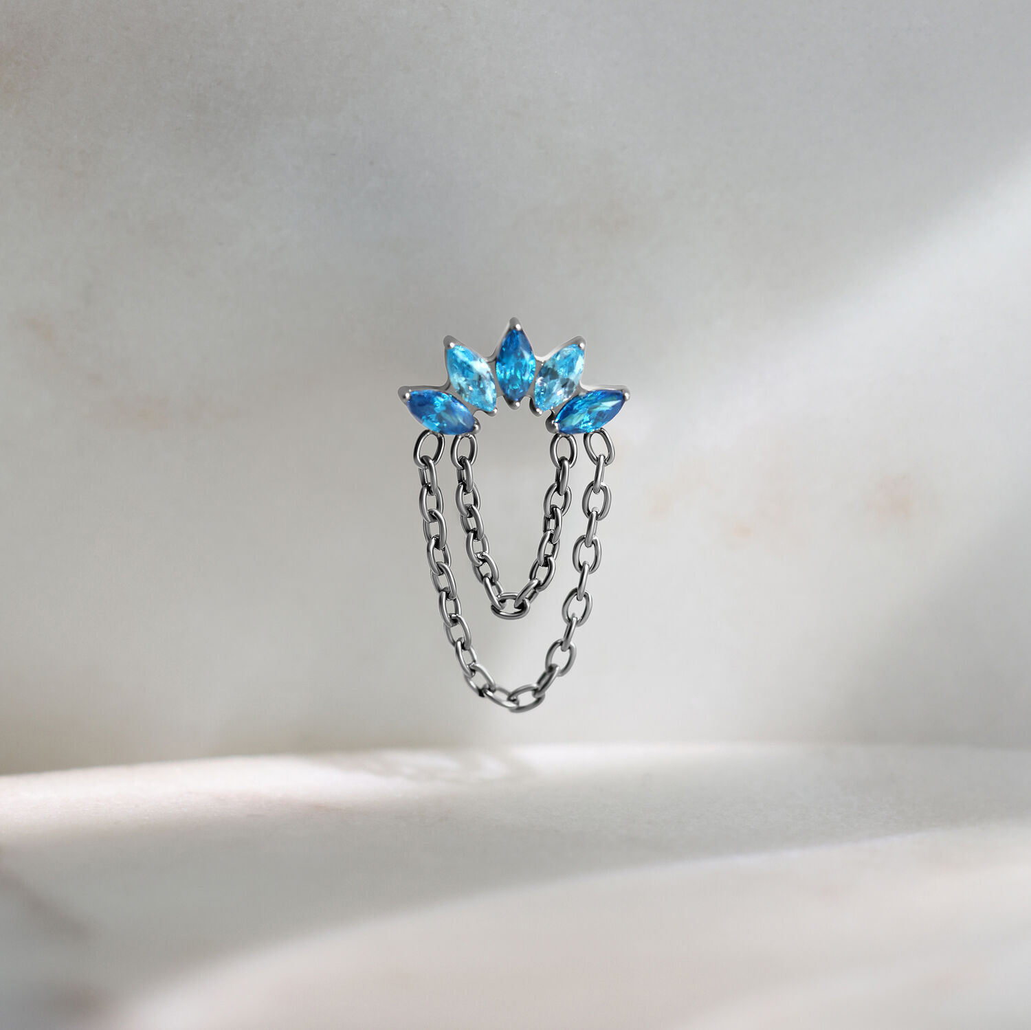 Silberfarbener Push Fit Piercing Aufsatz mit drei türkisfarbenen Kristallen auf hellem Hintergrund