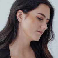 Frau mit langem, dunklem Haar trägt goldenen Pizza-Aufsatz im Ohr auf hellem Hintergrund