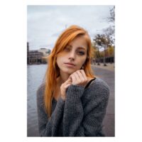 Junge Frau mit Nasenpiercing und grauem Pullover vor städtischem Hintergrund