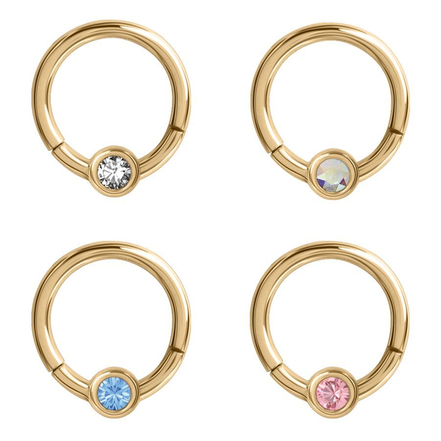 Vier goldene Piercing-Ringe mit klaren, blauen, rosa und schimmernden Kristallen auf weißem Hintergrund