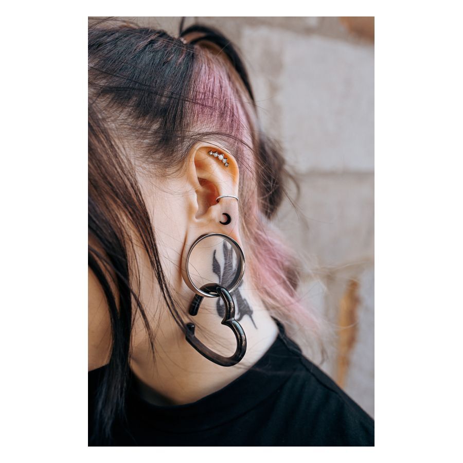 Nahaufnahme eines Ohres mit mehreren Piercings, darunter ein synthetischer Opalstein in Weiß.