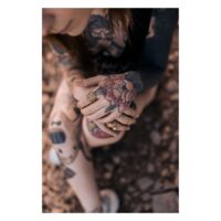 Goldener Boho-Ring in Blumenform an tätowierter Hand, sitzend auf Steinboden