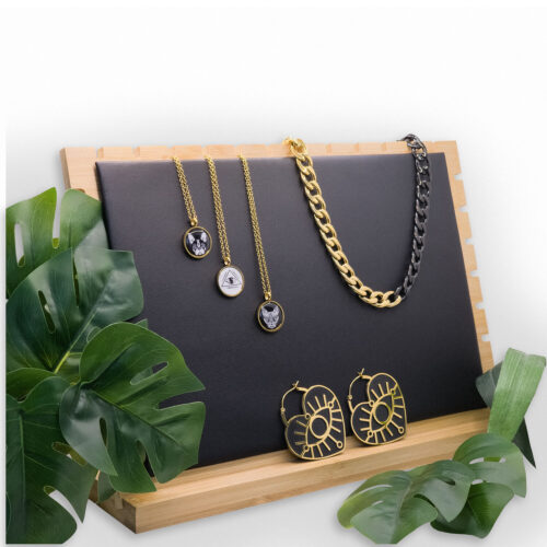 Schwarzer Display mit goldenen Ketten und Ohrringen auf Holzunterlage, umgeben von Pflanzen