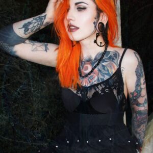 Frau mit orangefarbenem Haar und schwarzen Meow Hoops Ohrringen im Wald