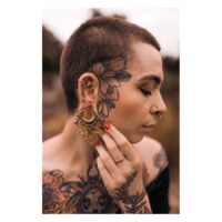 Person mit goldenen Mandala Labret Piercings und Tattoos auf Gesicht und Körper
