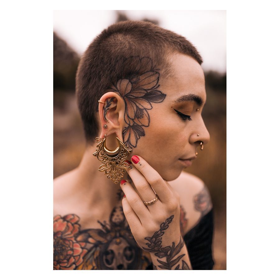 Person mit goldenen Mandala Labret Piercings und Tattoos auf Gesicht und Körper