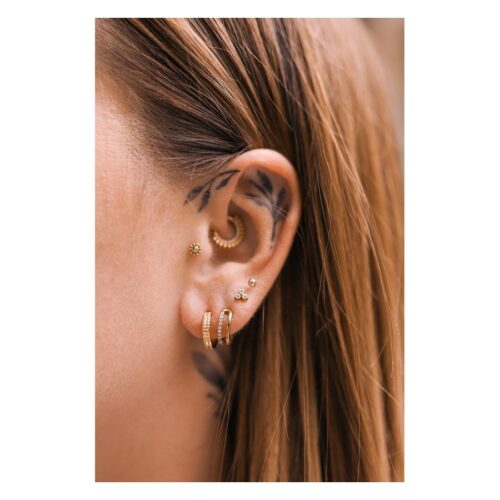 Ohr mit mehreren goldenen Piercings, darunter ein Rivet Clicker, auf hellem Hintergrund