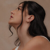 Frau mit 14K Gold Schneeflockenaufsatz im Ohr vor neutralem Hintergrund