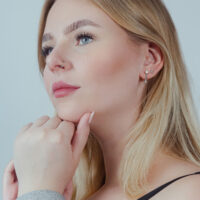 Frau trägt silbernen Doppelreihen Clicker im Ohr und Nasenring, neutraler Hintergrund