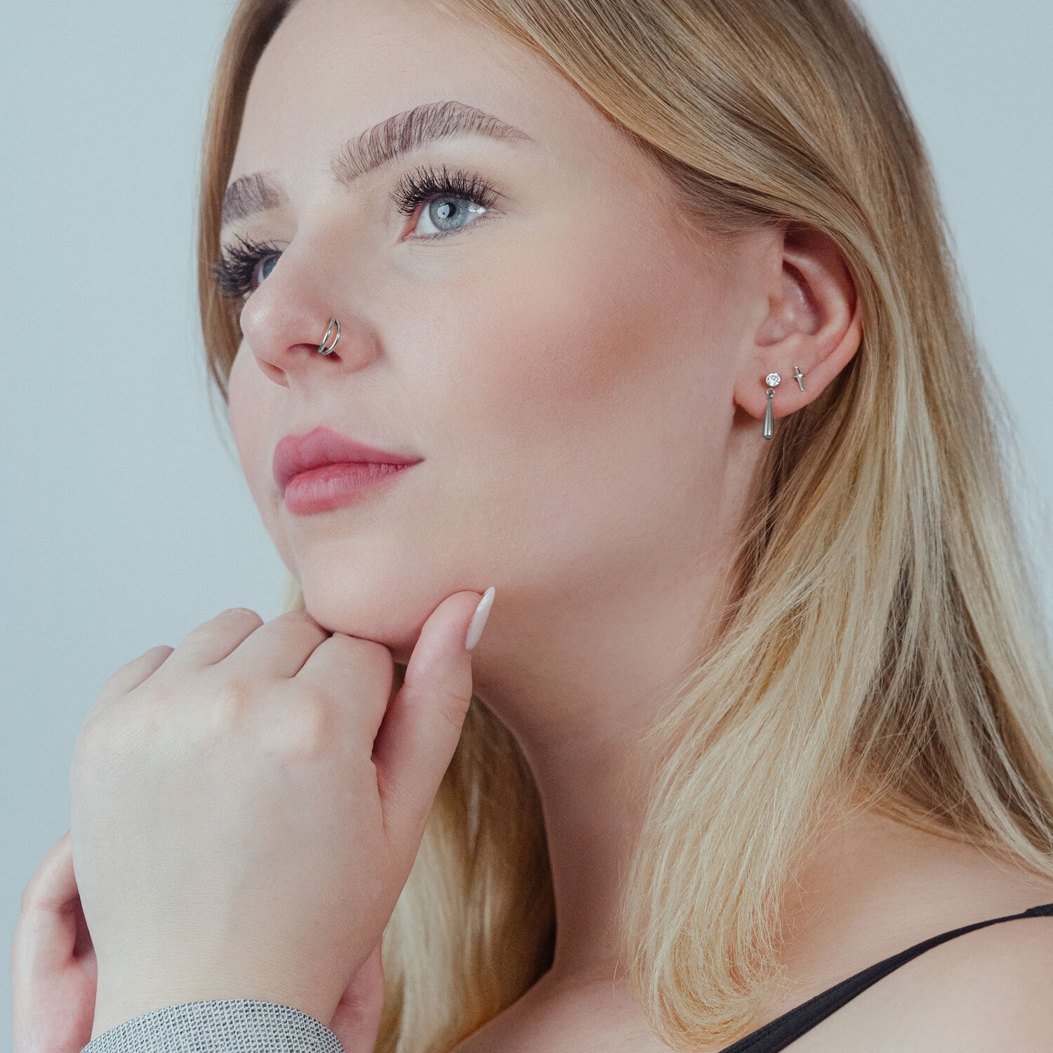 Frau trägt silbernen Doppelreihen Clicker im Ohr und Nasenring, neutraler Hintergrund