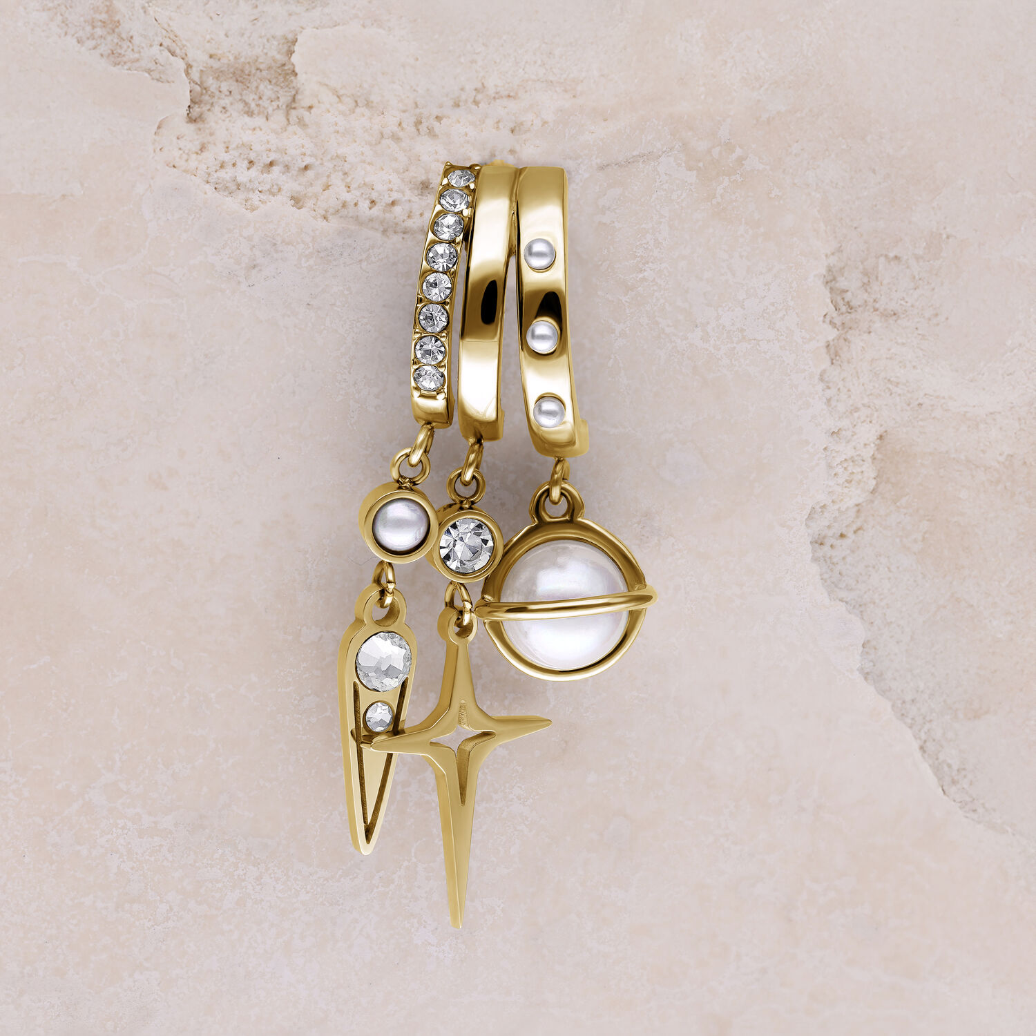 Goldene Ohrstecker mit Perlen und Glitzersteinen Drei goldene Ohrstecker mit Perlen, Glitzersteinen und Sternanhänger auf beigem Hintergrund