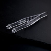 Zwei transparente, sterile Runde Piercingzangen liegen überkreuzt auf einem dunklen Hintergrund.