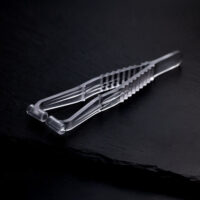 Transparente Septum Piercingzange aus Kunststoff auf dunklem, glattem Hintergrund