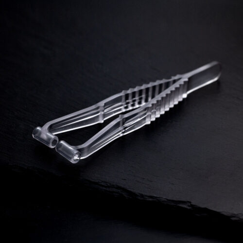 Transparente Septum Piercingzange aus Kunststoff auf dunklem, glattem Hintergrund