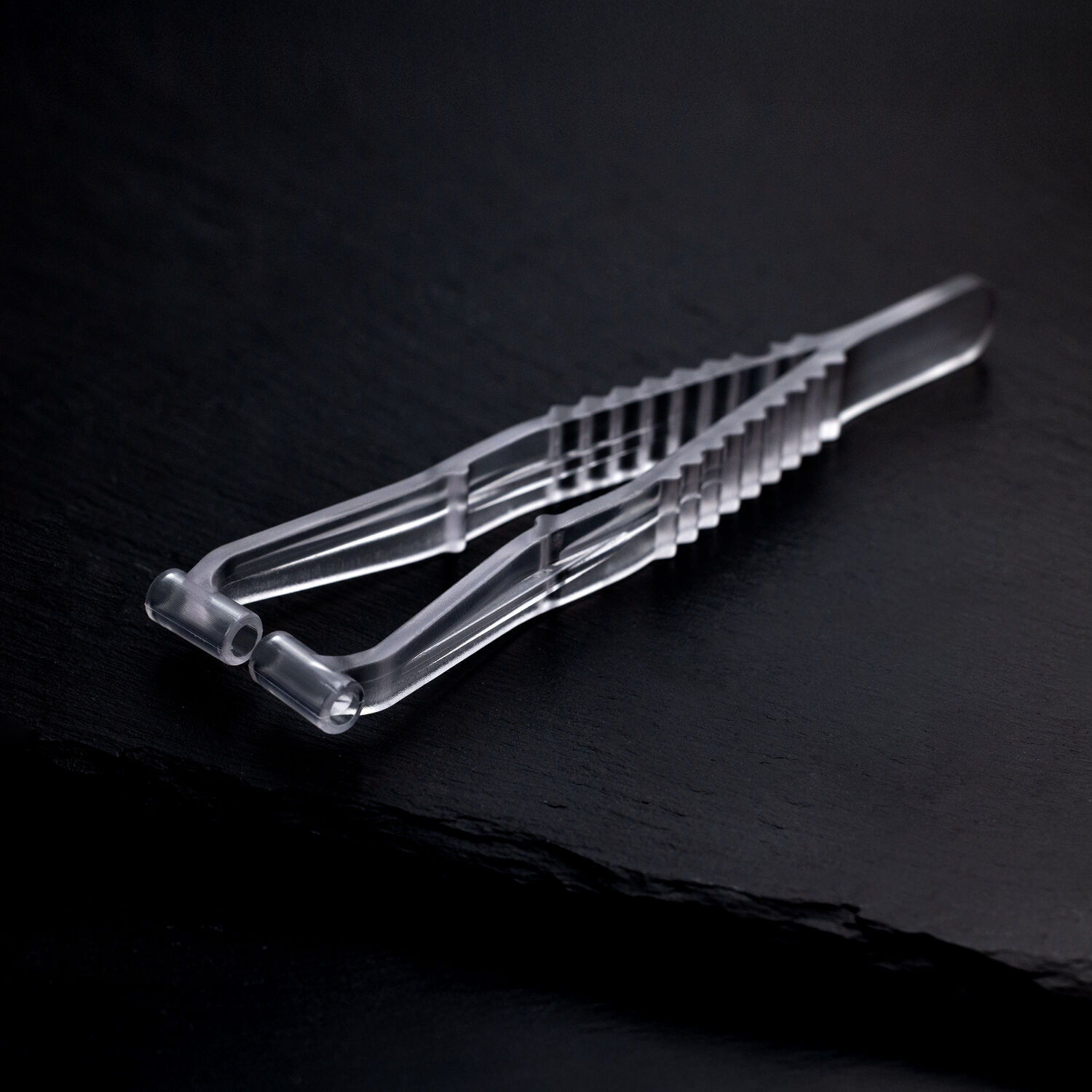 Transparente Septum Piercingzange aus Kunststoff auf dunklem, glattem Hintergrund