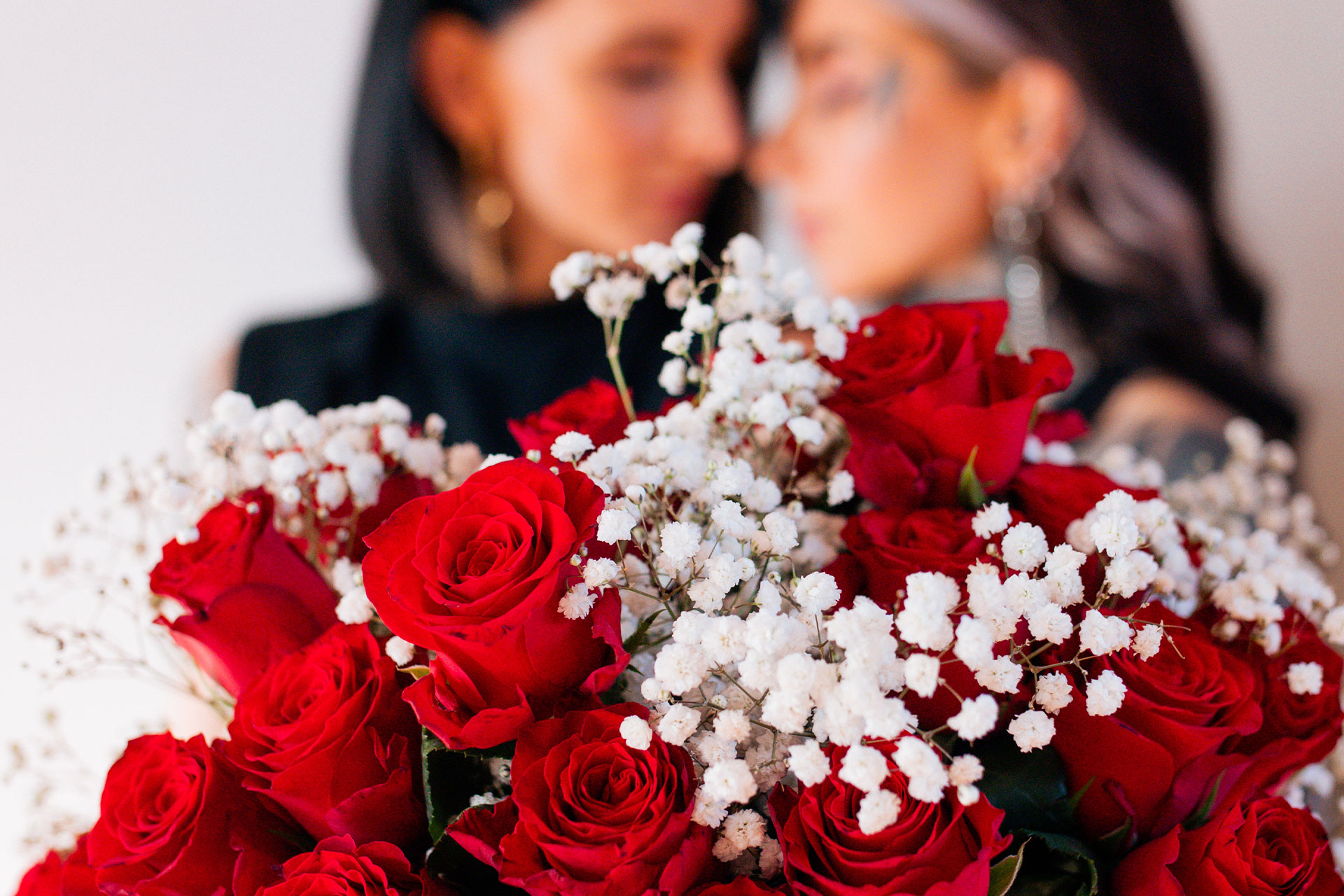 Nahaufnahme von roten Rosen und weißem Schleierkraut, unscharfer Hintergrund mit zwei Personen