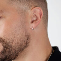 Silberne Creolen am Ohr eines Mannes mit Bart auf weißem Hintergrund