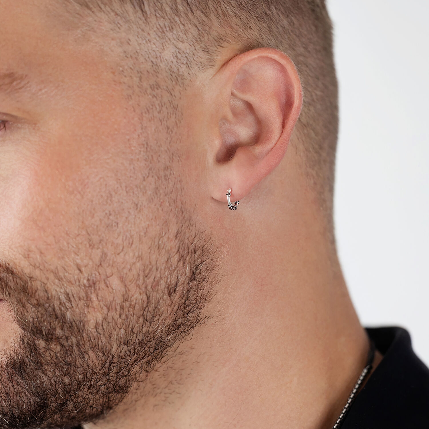 Silberne Creolen am Ohr eines Mannes mit Bart auf weißem Hintergrund