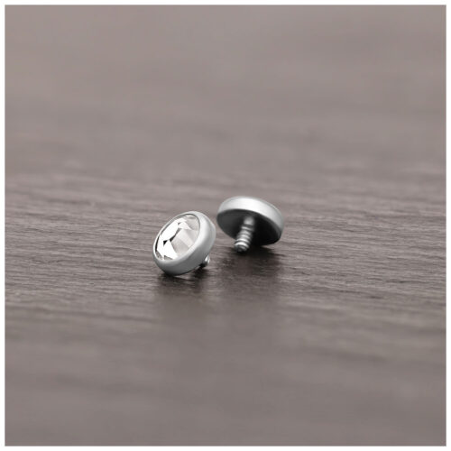 Silberner Piercing-Aufsatz aus Titan mit klarem Kristall auf Holzoberfläche liegend