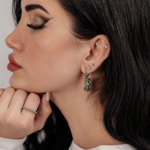 Frau mit silbernen Ohrhänger-Ohrringen und afrikanischem Türkis auf neutralem Hintergrund