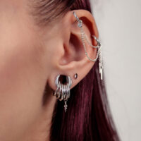 Nahaufnahme eines Ohres mit silberner Piercingkette und mehreren silbernen Ringen