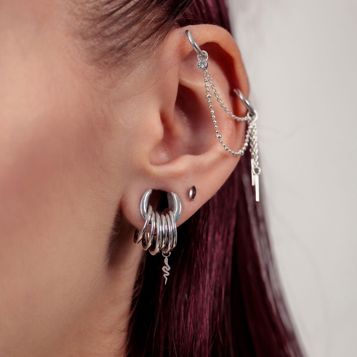Nahaufnahme eines Ohres mit silberner Piercingkette und mehreren silbernen Ringen