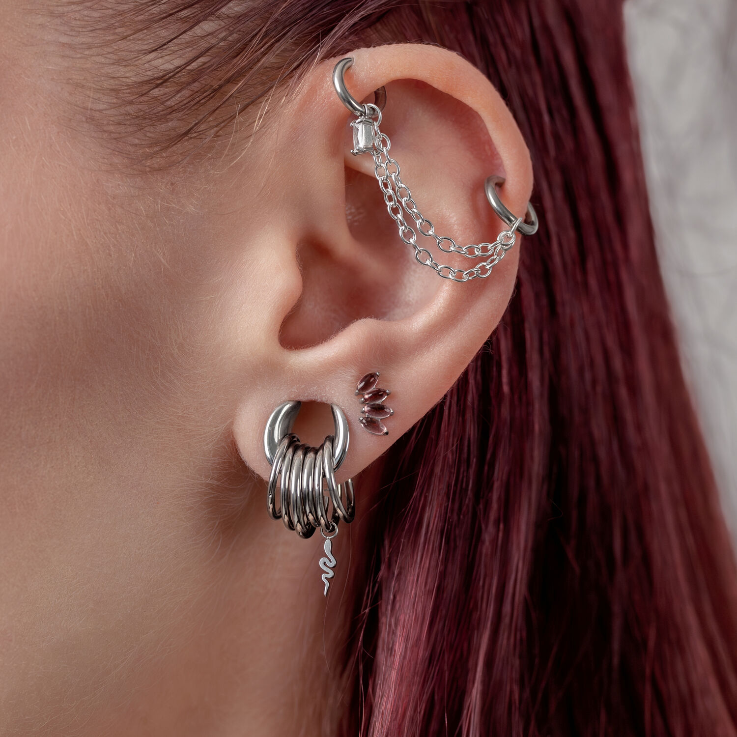 Ohr mit mehreren silbernen Piercings, darunter ein Schlangenanhänger, auf rotem Haar
