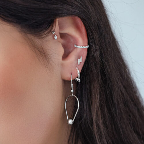 Nahaufnahme eines Ohres mit mehreren silbernen Piercings, einschließlich eines Kristallaufsatzes